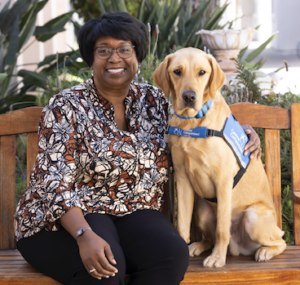 Woman seating on a bench next to a service dog